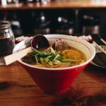 soup with vegetable beside chopsticks and glass of water